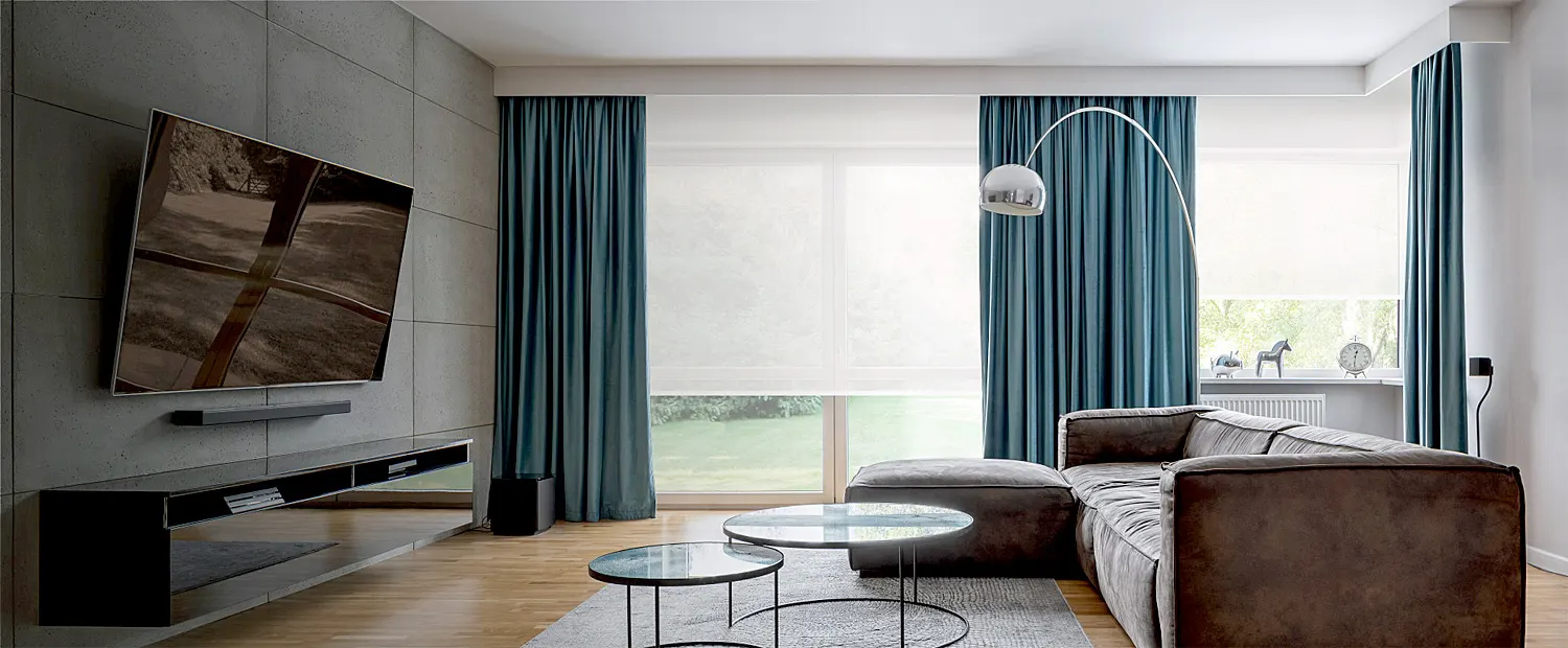 Modern residential living room with wide opaque roller shades and ripplefold overdrapes.